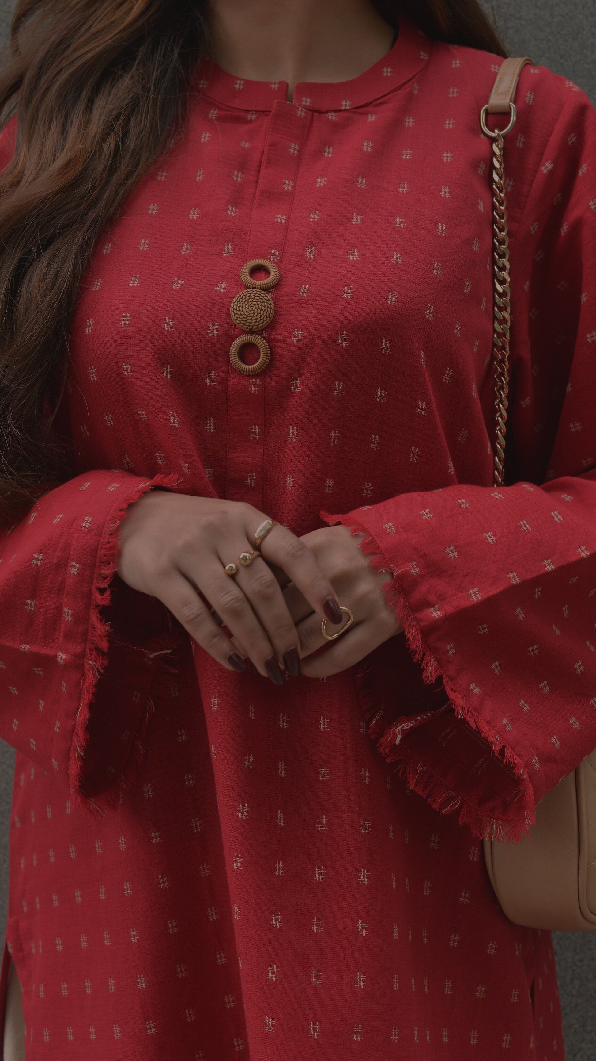 Red patterned dress with bell sleeves worn by a person, holding a beige handbag.